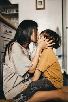 two people sitting on the floor kissing each other in front of a kitchen counter top