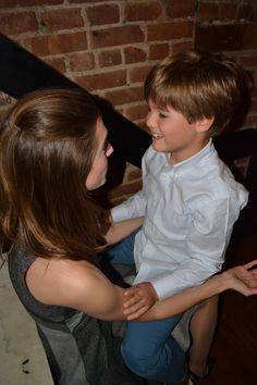 a young boy sitting on top of a woman's lap in front of a brick wall