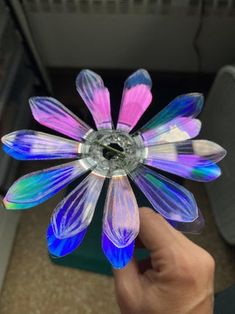 a hand holding a colorful glass flower in it's center with purple and blue petals