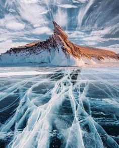 an ice covered mountain in the distance with water running through it and snow on the ground