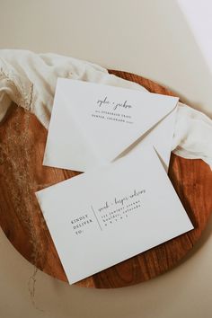 two white envelopes sitting on top of a wooden table next to an envelope with writing