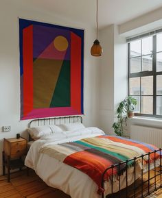 a bed sitting in a bedroom next to a window with a painting on the wall