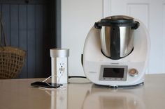 a white blender sitting on top of a counter next to a cup and an appliance