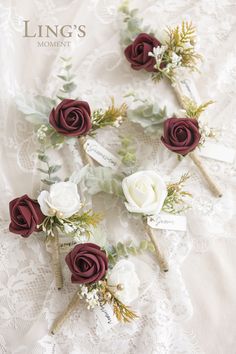 wedding boutonnieres with burgundy and white flowers are arranged on a lace tablecloth