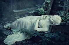 a white statue laying on top of a lush green forest