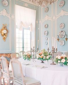 a dining room with blue walls and white table cloths, chandelier and plates on the wall