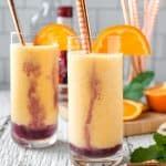 two glasses filled with drinks sitting on top of a table next to sliced oranges