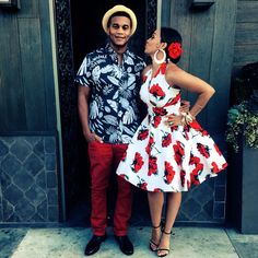 a man and woman standing in front of a door with red flowers on their dress