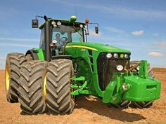 a green tractor parked in the middle of a field with two large tires on it