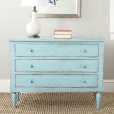 a blue dresser in a room with a white lamp and pictures on the wall behind it