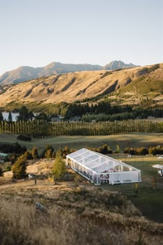 a large white building sitting on top of a lush green field next to mountains and trees