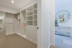 an empty walk - in closet with white cabinets and drawers on the wall, along with a large mirror