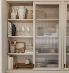 a white bookcase with glass doors and shelves filled with books, vases and other items