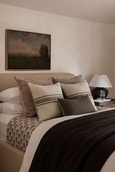 a bed with pillows and blankets on top of it next to a painting hanging above the headboard