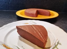 a piece of chocolate cake sitting on top of a white plate next to a yellow plate