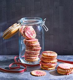 a glass jar filled with cookies next to a stack of cut - out cookies on a table