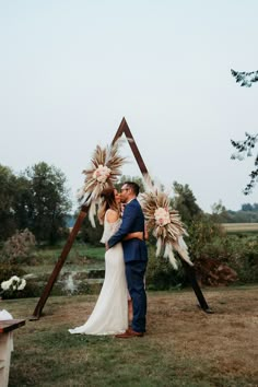 a bride and groom standing in front of an arch decorated with pamodia flowers