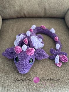 a crocheted purple and white dragon laying on top of a gray couch next to it's head