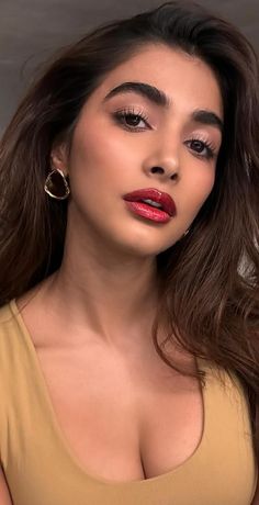 a woman with long brown hair and red lipstick wearing gold hoop earrings is posing for the camera