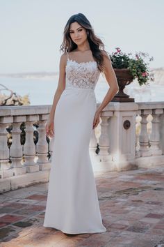 a woman in a white wedding dress standing on a stone walkway near the water and flowers