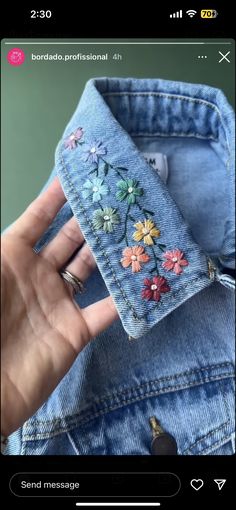 a hand is holding onto a jean jacket with embroidered flowers on the front and back