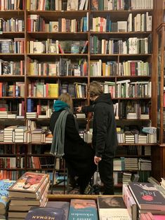 two people standing in front of a bookshelf filled with lots of different types of books