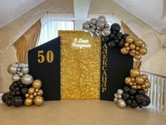 two large black and gold balloons are in front of a 50th anniversary book on the floor