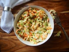 a white bowl filled with coleslaw and carrots next to a silver fork