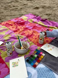 an artist's supplies are laid out on a blanket at the beach with watercolors and paints