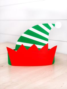 a green and red paper hat sitting on top of a wooden table next to a white wall