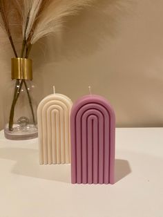 two candles sitting on top of a table next to a vase filled with dry grass