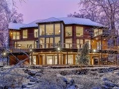 a large house is lit up in the winter with snow on the ground and trees around it