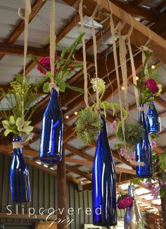 several blue vases with flowers hanging from them in a room filled with wood beams