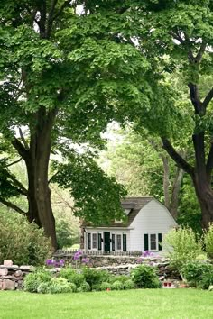 a white house surrounded by lush green trees and flowers in front of a stone wall