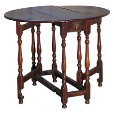 an old wooden table with turned legs and a small round top on one end, sitting against a white background