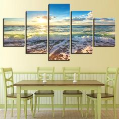 a dining room table with chairs and four paintings on the wall above it that have waves coming in to shore