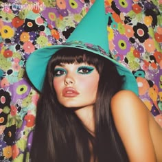 a woman with long black hair wearing a green hat and blue eyeshadow is laying down