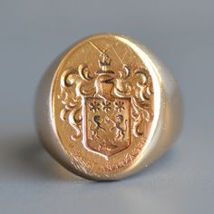 "A truly handsome vintage unisex armorial crest signet ring in solid 14k gold. this wonderful and weighty vintage signet ring features a hand engraved armorial crest on the oval front depicting a a sword topped knights helmet above a plaque with three stars and two dragons with flames in between them above water with a single fish and the Latin saying \"NEC ASPERA TERRENT\" in reverse below (meaning - They are not afraid of difficulties, or less literally \"Difficulties be damned.\" Motto for 27 Luxury Vintage Signet Ring With Center Stone, Luxury Vintage Signet Ring With Maker's Mark, Luxury Vintage Signet Ring With Hallmarks, Luxury Vintage Signet Ring, Insignia Ring, Signet Ring Design, Gcse Drama, Black Three Piece Suit, Mens Signet Ring