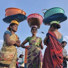 three women are carrying baskets on their heads