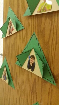 an origami cut out of green paper on a wooden surface with pictures hanging from it