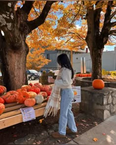 a woman standing next to a pile of pumpkins