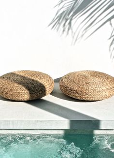 two woven baskets sitting on top of a pool next to a white wall and water