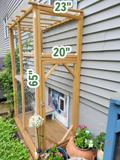 a small wooden bird cage sitting on the side of a house next to potted plants