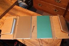 three notebooks sitting on top of a wooden table next to a drawer with drawers