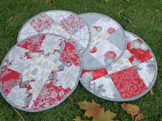 three red and white quilted placemats on green grass with leaves around them