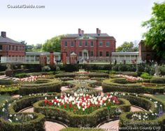 an elaborate garden in front of two large red brick buildings with white and red flowers