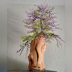 a wooden vase filled with purple flowers sitting on top of a blue table next to a white wall