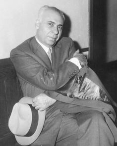 an old black and white photo of a man in a suit sitting on a couch