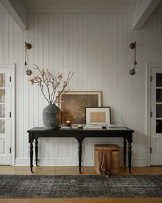 a room with a table, vase and pictures on the wall next to an open door