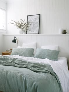 a bedroom with white walls and green linens on the bed, along with a plant